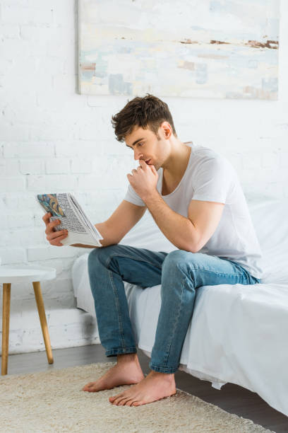 istock handsome man sitting on bed and reading newspaper at home 1165198996