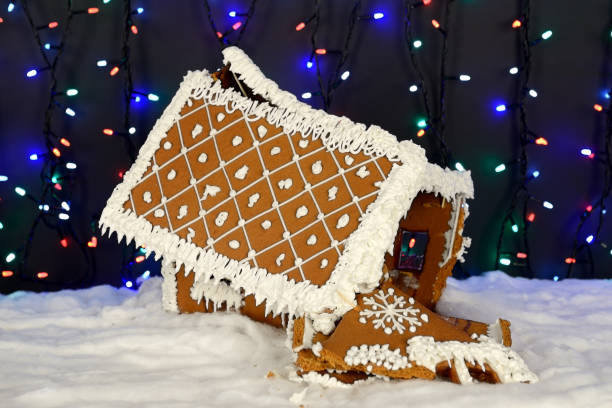 The crashed hand-made eatable gingerbread house, snow decoration, garland background illumination