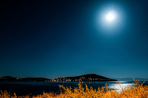 Night time moonlight shines on the sea, hills beyond and city lights / stars in the sky