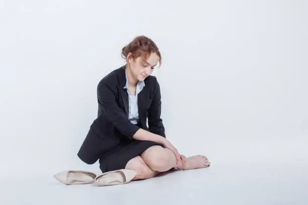 Woman in alcohol intoxication after corporate party. Girl wearing unbuttoned business jacket and takes off shoes from fatigue. Isolated white background