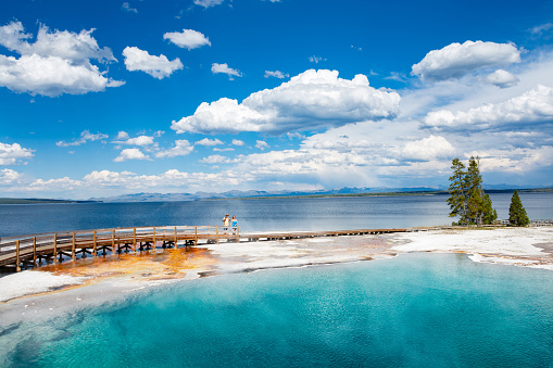 Couple relaxing and enjoying beautiful view of hot spring on vacation hiking trip. Beautiful Yellowstone Lake in the background and hot spring in foreground. Yellowstone National Park. Wyoming, USA