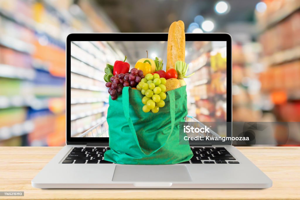 Supermarkt Gang verschwommenen Hintergrund mit Laptop-Computer und grüne Einkaufstasche auf Holz Tisch Lebensmittel Online-Konzept - Lizenzfrei Internet Stock-Foto