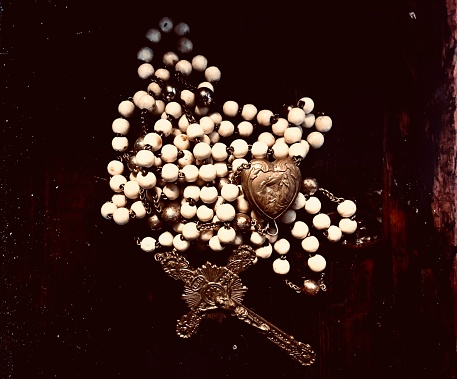 Closeup of off white rosary beads with a brass locket and cross engraved with the figure of Christ. Beads are on an antique varnished wooden table