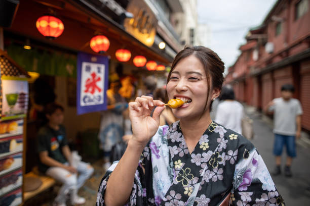 junge frau in yukata essen japanische dango knödel auf der straße - japanische küche stock-fotos und bilder