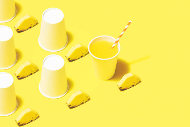 Disposable paper cups on color background. Pineapple juice flat lay on yellow background.