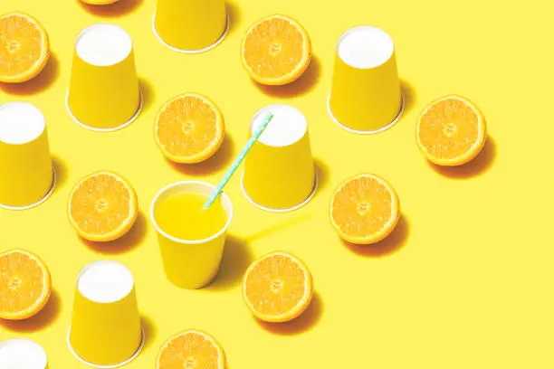 Photo of Orange juice and yellow paper cups flat lay on yellow background