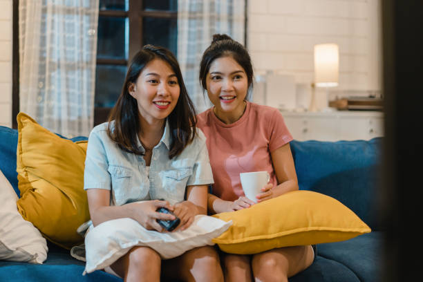 lesbian lgbt women couple watching television at home, asian female lover feeling happy funny moment looking drama entertainment together on sofa in living room in night concept. - apartment television family couple imagens e fotografias de stock