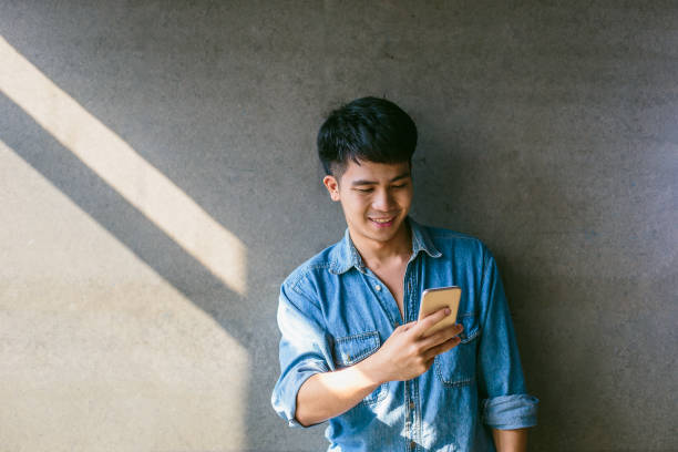 istock Young Asian man using smart phone on concrete gray background at office 1165244439
