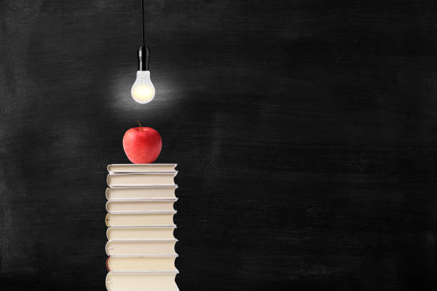 Light bulb over the apple on piled-up books against blackboard with copy space.