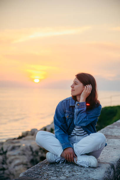 istock young pretty woman sitting at cliff looking on beautiful sunset 1165252230