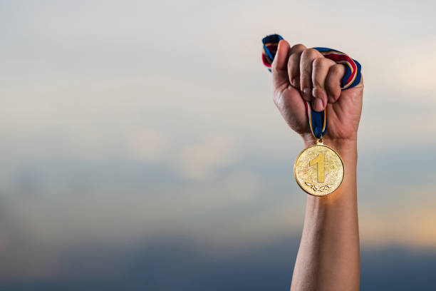 Hand holding gold medal on against cloudy twilight sky background