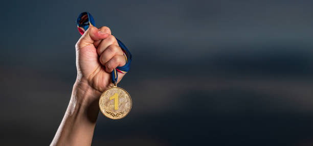 istock Hand holding gold medal on against cloudy twilight sky background 1165256788