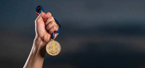 Hand holding gold medal on against cloudy twilight sky background, The winner and successful concept