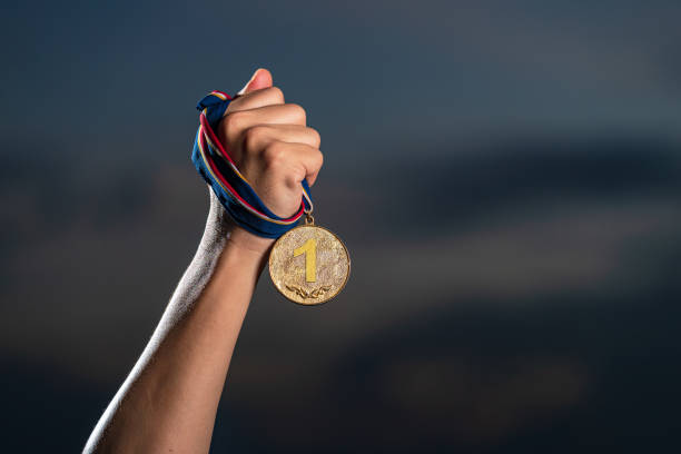 istock Hand holding gold medal on against cloudy twilight sky background 1165256792
