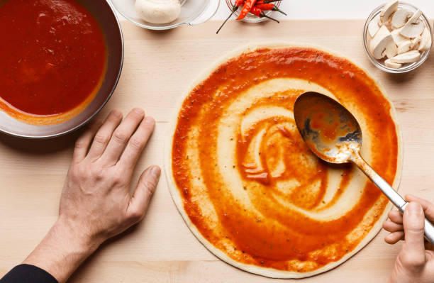 chef cocinando pizza, esparciendo salsa de tomate en la base de la pizza - food industry manufacturing human hand fotografías e imágenes de stock