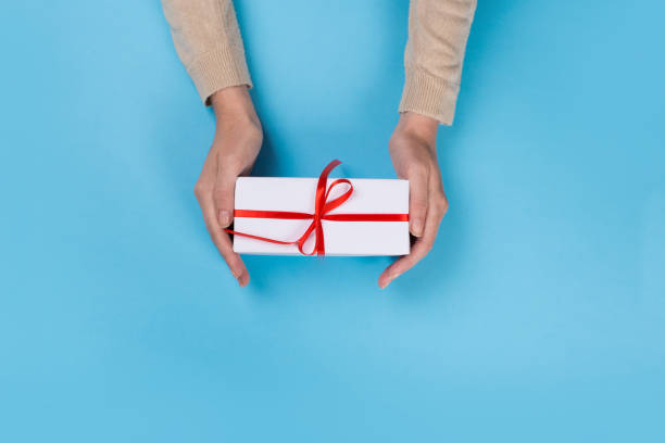 istock Womans hands holding gift or present box on blue pastel table top view. Flat lay  for birthday or New Year. 1165263140