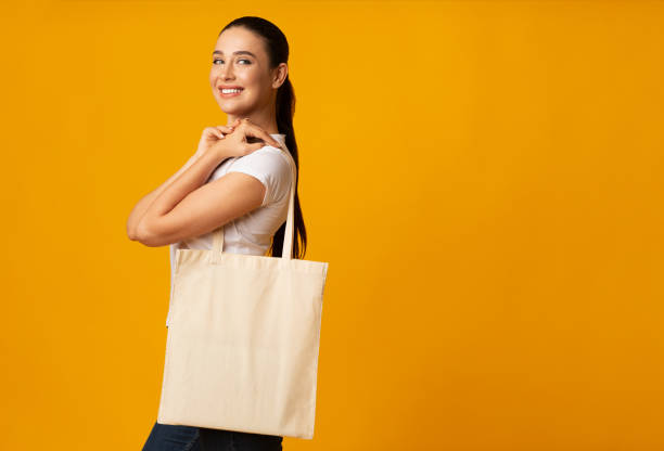 ragazza che tiene in mano una borsa ecologica bianca bianca su sfondo giallo - recycled bag foto e immagini stock