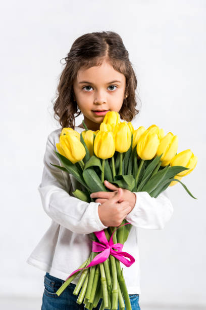 istock Front view of cute curly kid holding tulips bouquet on white 1165269106