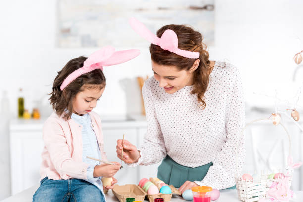 istock Joyful mother and daughter in bunny ears painting easter eggs in kitchen 1165269410