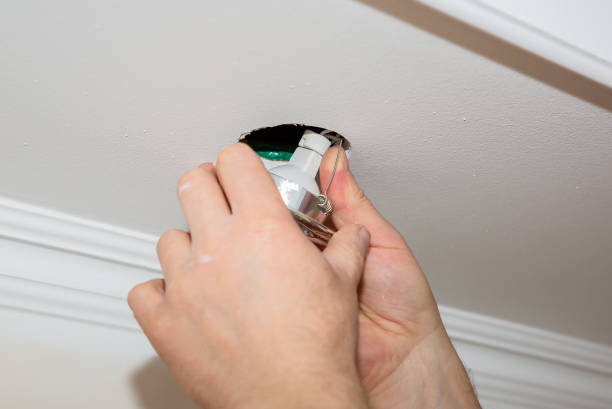 istock Man is installing electrical light bulb in the ceiling. Maintenance repair works in the flat. Restoration indoors. 1165277571