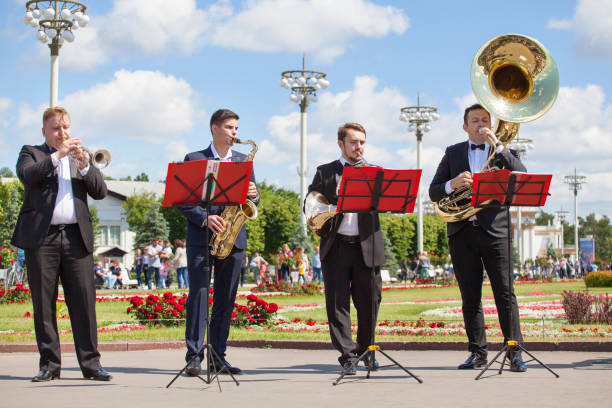 nova vida banda de latão, vento jogadores instrumento musical, orquestra executa música, quatro homens músicos jogam trompete, saxofone, trompa francesa, sousaphone no verão vdnkh parque - brass band french horn brass instrument music - fotografias e filmes do acervo