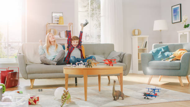 istock At Home: Smart Boy Playing in Video Game Console, Using Joystick Controller, His Older Sister Sits Near on Sofa and Cheers for Him. They Win and Celebrate Happily. Happy Children Playing Videogames. 1165279379