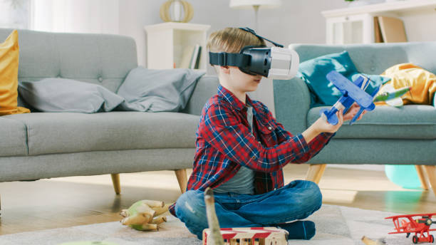 istock Smart Little Boy Wearing Virtual Reality Headset Plays with Toy Airplane while Sitting on a Carpet in His Living Room. Happy Child Uses Futuristic AR Glasses at Home. 1165279494