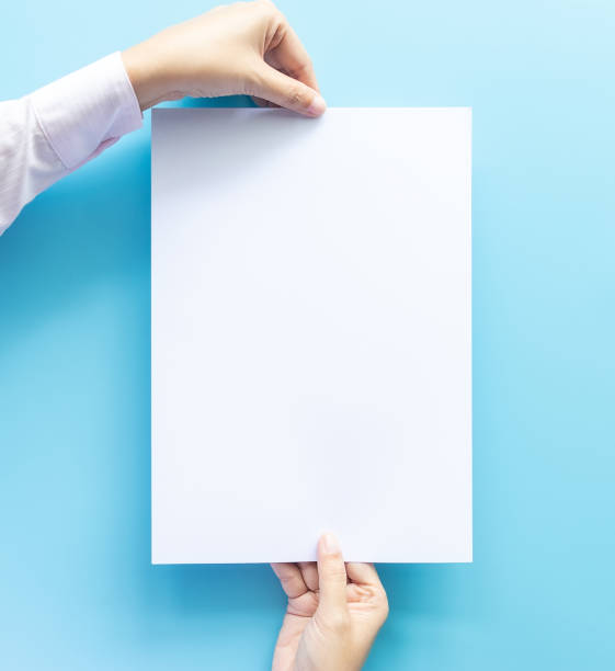 istock close up of two hands holding  empty white blank letter paper size A4 with copy space for flyer or invitation mock up isolated on a blue background. 1165287189