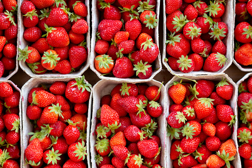 Many fresh strawberries in boxes for sale at a fruit market outdoors. Top view. Healthy food.
