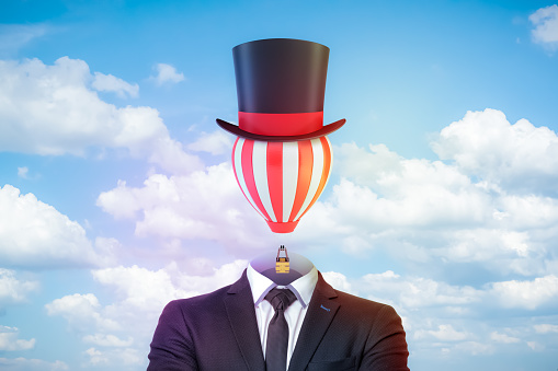 Male figure in smart suit, tie and tophat with a striped hot-air balloon instead of the head against blue sky with white clouds. Ideas change world. Broaden your mind. Creativity and flight of fancy.