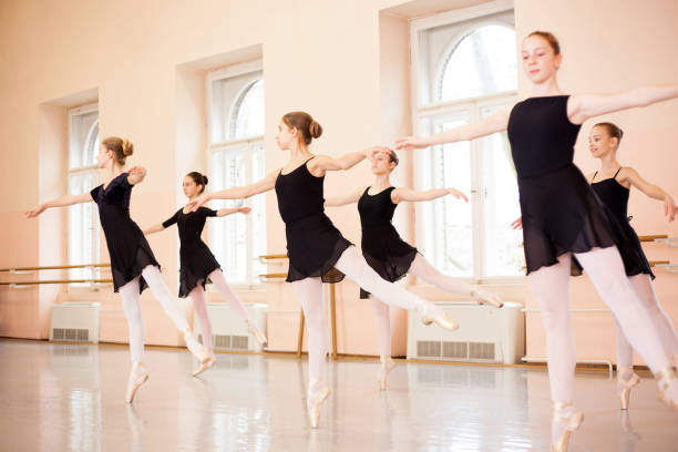 gruppo medio di ragazze adolescenti in abiti neri che praticano mosse di balletto in un grande studio di danza - scuola di danza classica foto e immagini stock