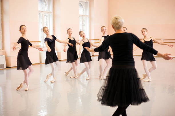 Senior ballet instructor demonstrating moves in front of a group of teenage girls Senior ballet instructor demonstrating moves in front of a group of teenage girls. Practicing classical ballet in a large dancing studio. dance studio instructor stock pictures, royalty-free photos & images