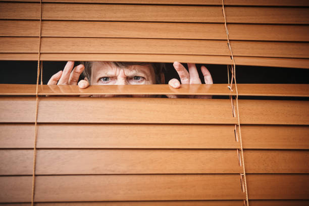 istock Alarmed and suspicious, senior woman peeps through blinds 1165292829
