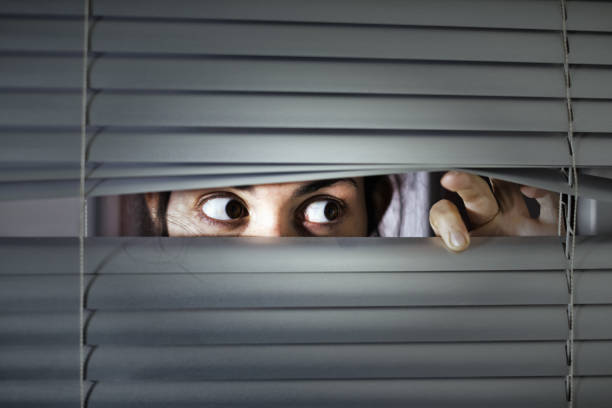 istock Terrified young woman peeping sideways through venetian blind 1165293261