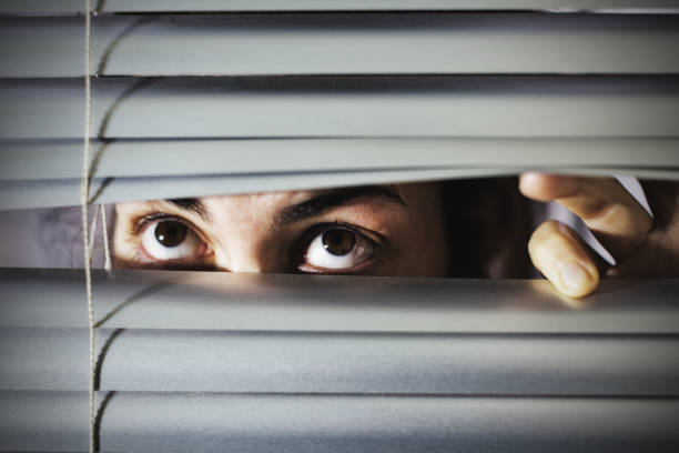 istock Nervous young brunette looks upwards through venetian blind slats 1165294207