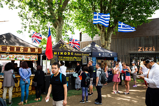 London, UK - 30 June, 2019: color image depicting crowds of people perusing and sampling the food from a range of different stalls at an outdoor food market in London, UK. The range of different cuisine on offer includes Greek, Indian, Brazilian and Mexican. Each of the food stalls has its country's flag flying proudly above it.