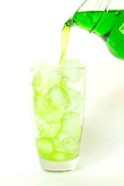 Summer drink; pouring green soda in glass with dancing bubbles on ice cubes isolated on white background