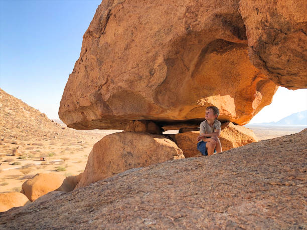 Young boy sitting under a natural arch at Spitzkoppe Namibia Africa