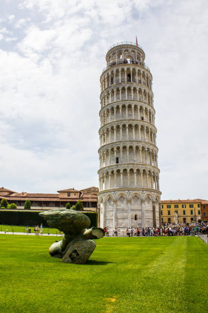 Pisa Italy Pisa, Italy - July 9, 2017: The Fallen Angel Sculpture in Piazza dei Miracoli with Leaning Tower of Pisa in the Background. pisa leaning tower of pisa tower famous place stock pictures, royalty-free photos & images