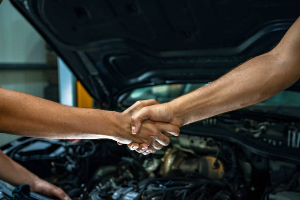 Car mechanic handshakes customer Caucasian young mechanic shaking hands with a mature male customer in front of a car. Photo of a  man giving an handshake in an industrial facility. Man greets auto master. Concept - car service. Handshake. auto mechanic photos stock pictures, royalty-free photos & images