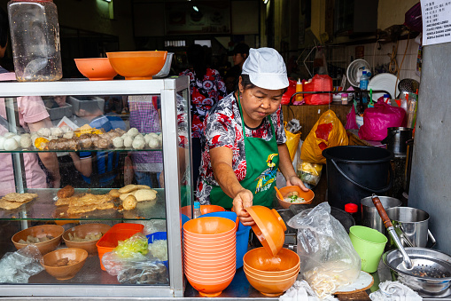 IPOH, MALAYSIA - DECEMBER 11: Woman serves up noodles for clients on a food court of Ipoh on December 11, 2018 in Ipoh, Malaysia.