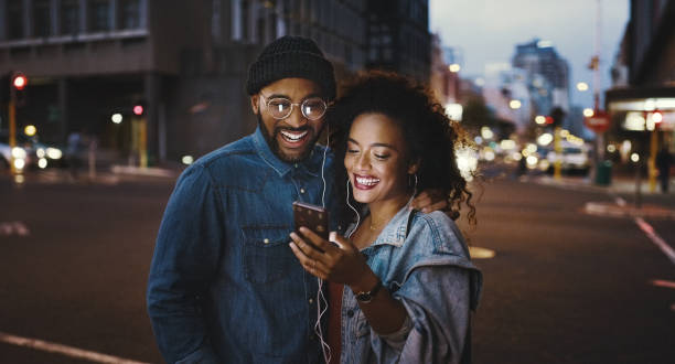 Getting the night started with some awesome music Shot of a young couple using a smartphone and earphones in the city date night romance stock pictures, royalty-free photos & images