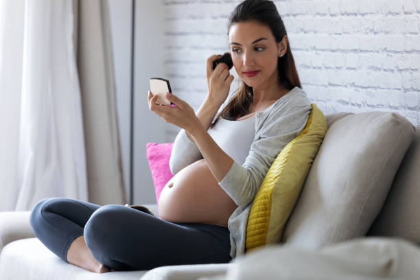 istock Beautiful pregnant young woman doing her makeup while sitting on sofa at home. 1165320282