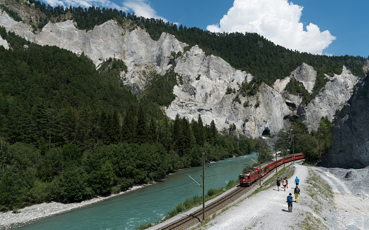 Versam, GR / Switzerland - 30. July 2019: hikers and the Rhaetian railway on the banks of the Rhine River in the Ruinaulta Gorge in the Swiss Alps
