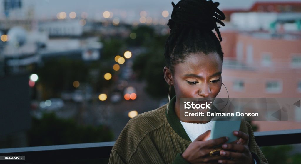 Stay connected and don't get left in the dark Shot of an attractive young woman using a smartphone in the city African Ethnicity Stock Photo