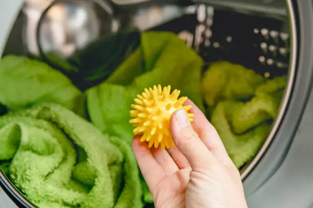 Photo of Using pvc dryer balls is natural alternative to both dryer sheets and liquid fabric softener, balls help prevent laundry from clumping in the dryer.  Woman hand put in a yellow spiky dryer ball.
