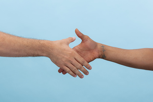 Closeup shot of human holding hands isolated on blue studio background. Concept of human relations, friendship, partnership, business or family. Copyspace.
