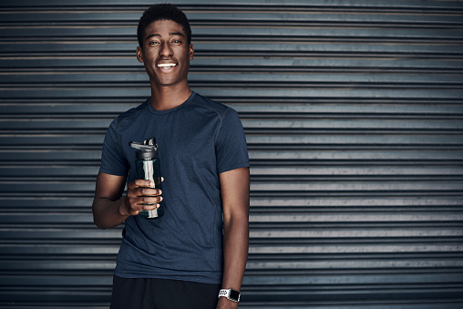 Cropped portrait of a handsome young man standing and holding a water bottle before working out against a dark background