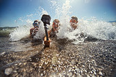 Kids playing in sea waves and filming themselves using waterproof action camera.