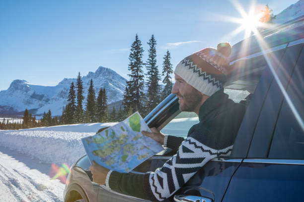 Young man looks at road map from insider car on snowy mountain road- road trip Young man in car on mountain road looks at map for directions. Mountain landscape in winter with snow covering road and pine trees. road map of canada stock pictures, royalty-free photos & images